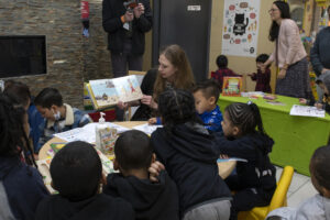 Chelsea Clinton sits at a table with children holding up a book