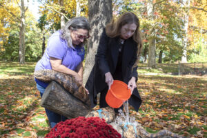 Chelsea Clinton and another individual stand outside and pour water from an orange bucket