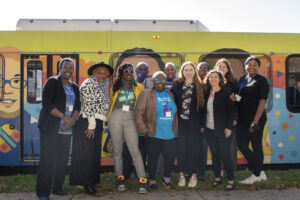 Chelsea Clinton and ten individuals pose in front of a colorful bus