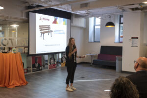 Chelsea Clinton speaks in front of a group, with a presentation screen behind her