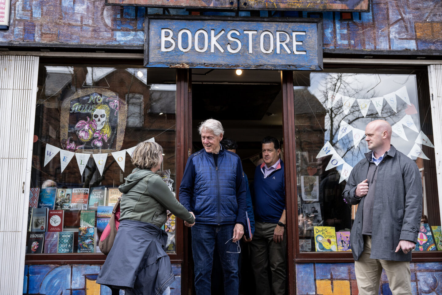 President Clinton stands in the doorway of a bookstore while greeting an individual with a handshake
