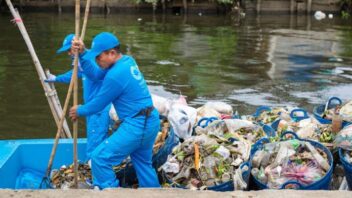 Two people stand in a boat filled with trash as they remove waste from a body of water.