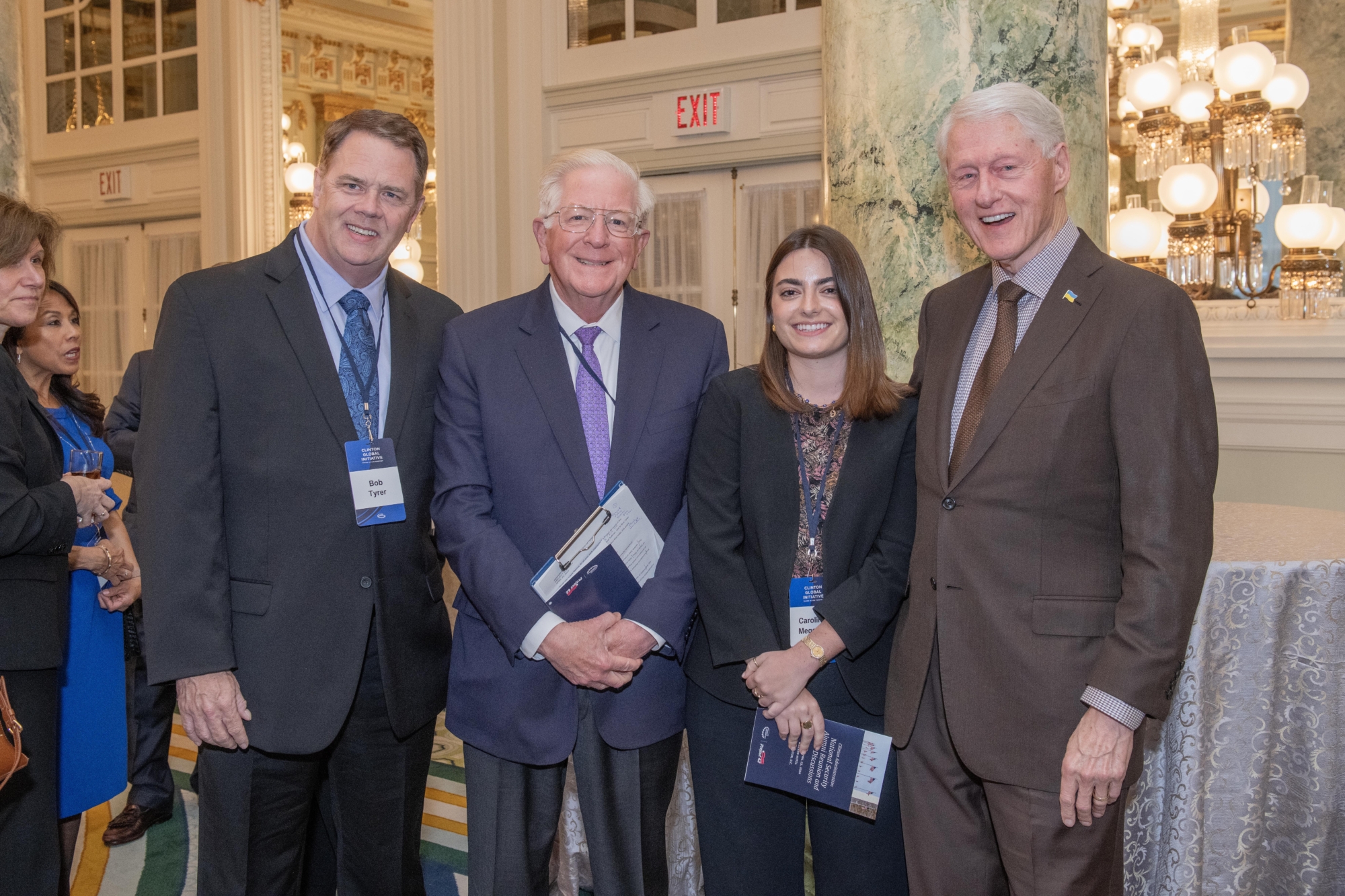 President Clinton stands with event hosts while smiling.